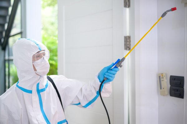 A medical staff in PPE suit is using disinfectant spray in living room, Covid-19 protection , disinfection concept .