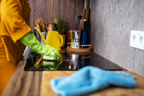Cooktop cleaning person with green gloves in kitchen. Household chores. Housekeeping hygiene and domestic lifestyle concept