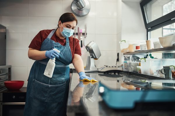Hard-working cafe staff with spray bottle and cloth following safety protocols by cleaning and sanitizing surfaces