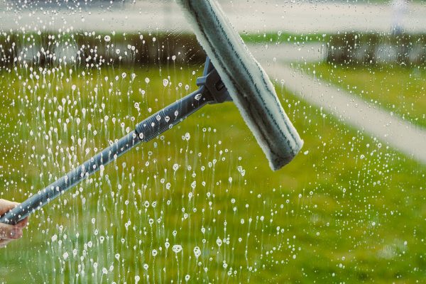 Washing windows with glass cleaner and mop. Woman from a window cleaning company washes windows in the house. House cleaning with window washing. Mop for washing glass.